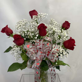 Red roses with white baby's breath in a glass vase, tied with a heart ribbon