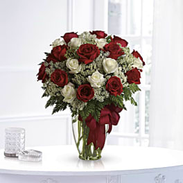 Red and white roses arranged in a clear glass vase with a red ribbon