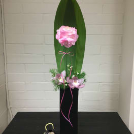 Tall floral arrangement with pink blooms, orchids, and a large green leaf in a black vase