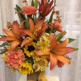 Tall bouquet of orange lilies, sunflowers, and carnations in a burlap-wrapped vase