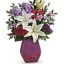 Bouquet of white lilies, pink roses, and purple flowers in a purple vase