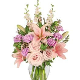 Pink lilies and roses arranged in a clear glass vase