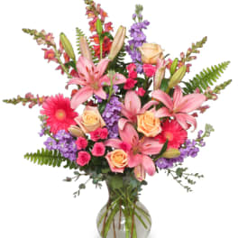Mixed bouquet of pink lilies, roses, and purple flowers in a glass vase