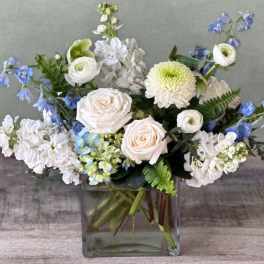 White and blue mixed flower arrangement in a square glass vase
