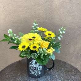Yellow flowers arranged in a black mug with a sun-themed message