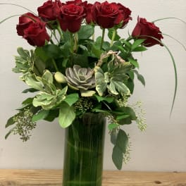 Red roses and succulents arranged in a tall green glass vase