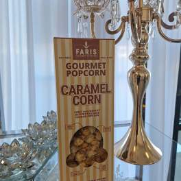 Box of caramel gourmet popcorn on a mirrored table beside a gold candelabra
