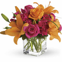 Pink roses and orange lilies arranged in a clear glass vase