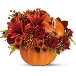 Autumn floral arrangement in a pumpkin container with red and orange blooms