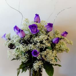Purple roses in a glass vase with white filler flowers