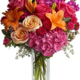 Bright mixed bouquet of roses, lilies, and hydrangea in a clear vase