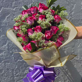 Bouquet of pink roses with white filler flowers and a purple ribbon