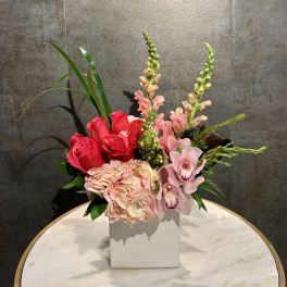 Pink roses and orchids arranged in a white square vase