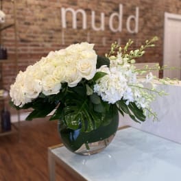 White roses and orchids in a round glass vase