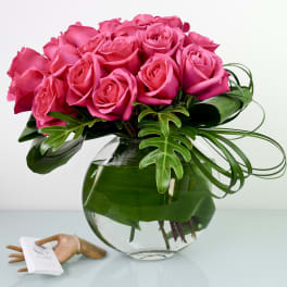 Pink roses arranged in a clear glass vase with tropical leaves