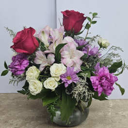 Mixed bouquet of roses, lilies, and purple flowers in a glass vase