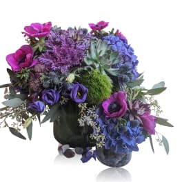 Purple and blue floral arrangement with succulents in a dark vase