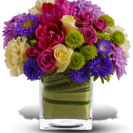Mixed bouquet of roses, tulips, and daisies in a clear glass vase