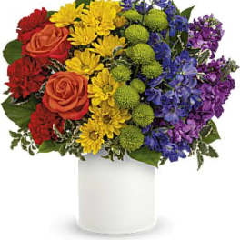 Rainbow bouquet of roses, daisies, and purple flowers in a white vase
