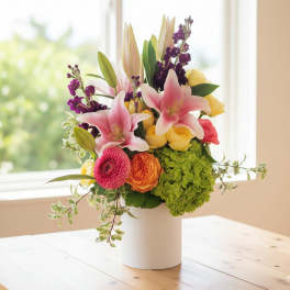 Mixed bouquet of pink lilies, roses, hydrangea, and gerbera daisy in a white vase