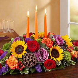 Low floral centerpiece with lit orange candles and sunflowers