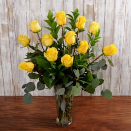 Tall arrangement of yellow roses in a clear glass vase on a wooden table
