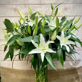 Tall arrangement of white lilies with buds in a clear green glass vase