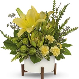 Yellow lilies and green protea in a white planter on wooden legs