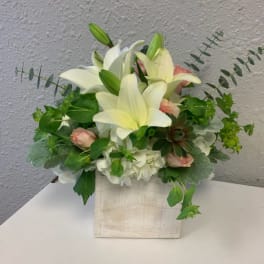 White lilies and pale pink roses arranged in a square vase