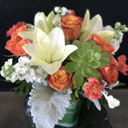 Bouquet of orange roses, white lilies, and a green succulent in a vase