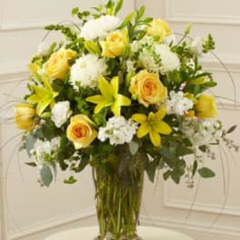Yellow roses and lilies arranged with white blooms in a clear glass vase.
