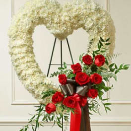 White floral heart wreath with red roses and ribbon on a stand