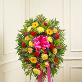 Standing floral wreath with bright mixed flowers and a pink ribbon bow