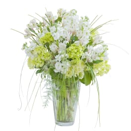 Tall arrangement of white and green flowers with wispy grass in a clear glass vase
