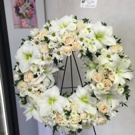 White floral wreath on a stand with cream roses and lilies