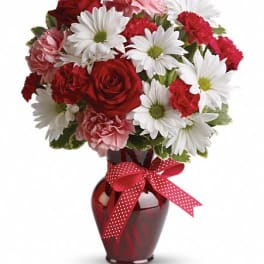 Bouquet of red roses, white daisies, and pink carnations in a red vase with ribbon