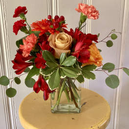 Mixed bouquet of red, orange, and peach flowers in a glass vase