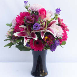 Mixed bouquet of pink, purple, and white flowers in a black vase