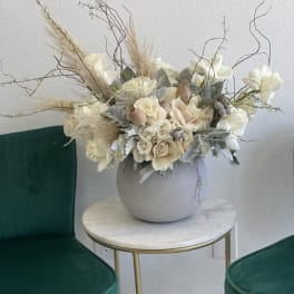 Cream floral arrangement in a round gray vase with tall dried branches