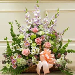 Basket arrangement of pink roses and purple flowers with a peach ribbon