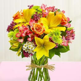 Bouquet of yellow lilies and mixed pink flowers in a glass vase