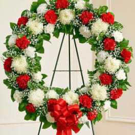 Heart-shaped wreath of red and white carnations on an easel with a red bow