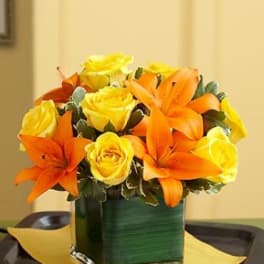 Orange lilies and yellow roses arranged in a square glass vase