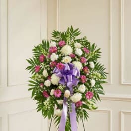 Standing floral wreath with white and pink flowers and a purple ribbon
