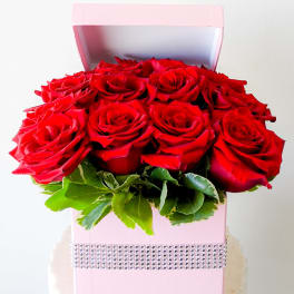 Red roses arranged in a pink gift box with a rhinestone band