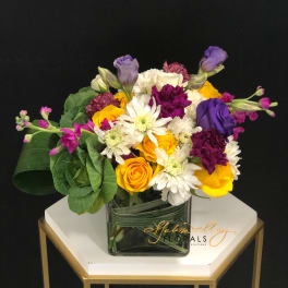 Mixed bouquet of yellow, white, purple, and pink flowers in a glass vase