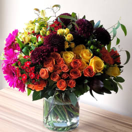 Mixed bouquet of roses, chrysanthemums, and lilies in a clear glass vase