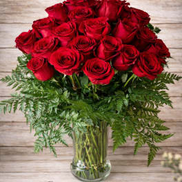Bouquet of red roses in a clear glass vase with fern foliage