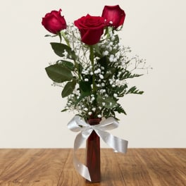 Three red roses in a tall vase with baby's breath and a white ribbon