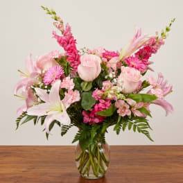 Pink lilies, roses, and gerbera daisies in a clear glass vase